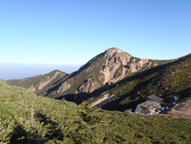 朝、西天狗岳と根石山荘（手前）。左奥には北アルプスが見える 