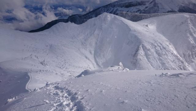 西天狗からのながめ　硫黄岳の手前、雪で埋まったように見える山荘は、根石岳山荘です