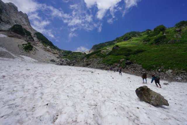 夏空のもと、大雪渓を登る登山者　