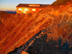モルゲンロートに照る山荘。長く延びた小石の影が動き出し、稜線はドラマチックな紅色に包まれます。