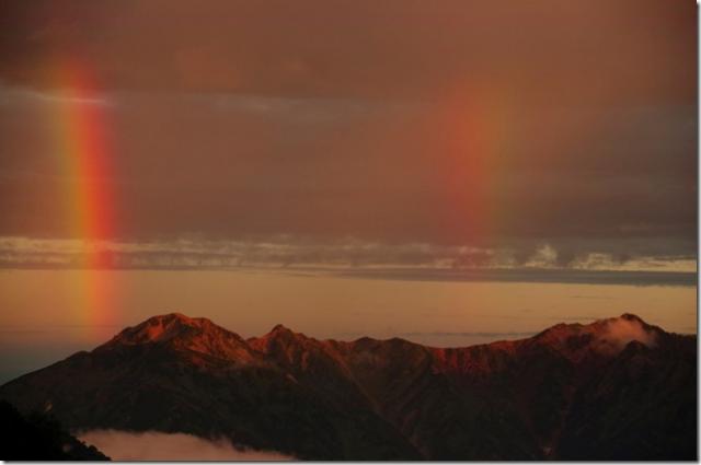 ヒュッテの窓から見える鷲羽岳の左とワリモ岳～水晶岳の稜線から２本の鮮やかな虹が出現。