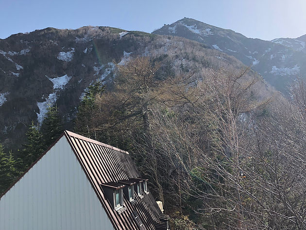 小屋の裏からの山頂方面　逆光でわかりにくいですが、三角形のピークの下に見えるなだらかな斜面が、最も残雪の多いところです。